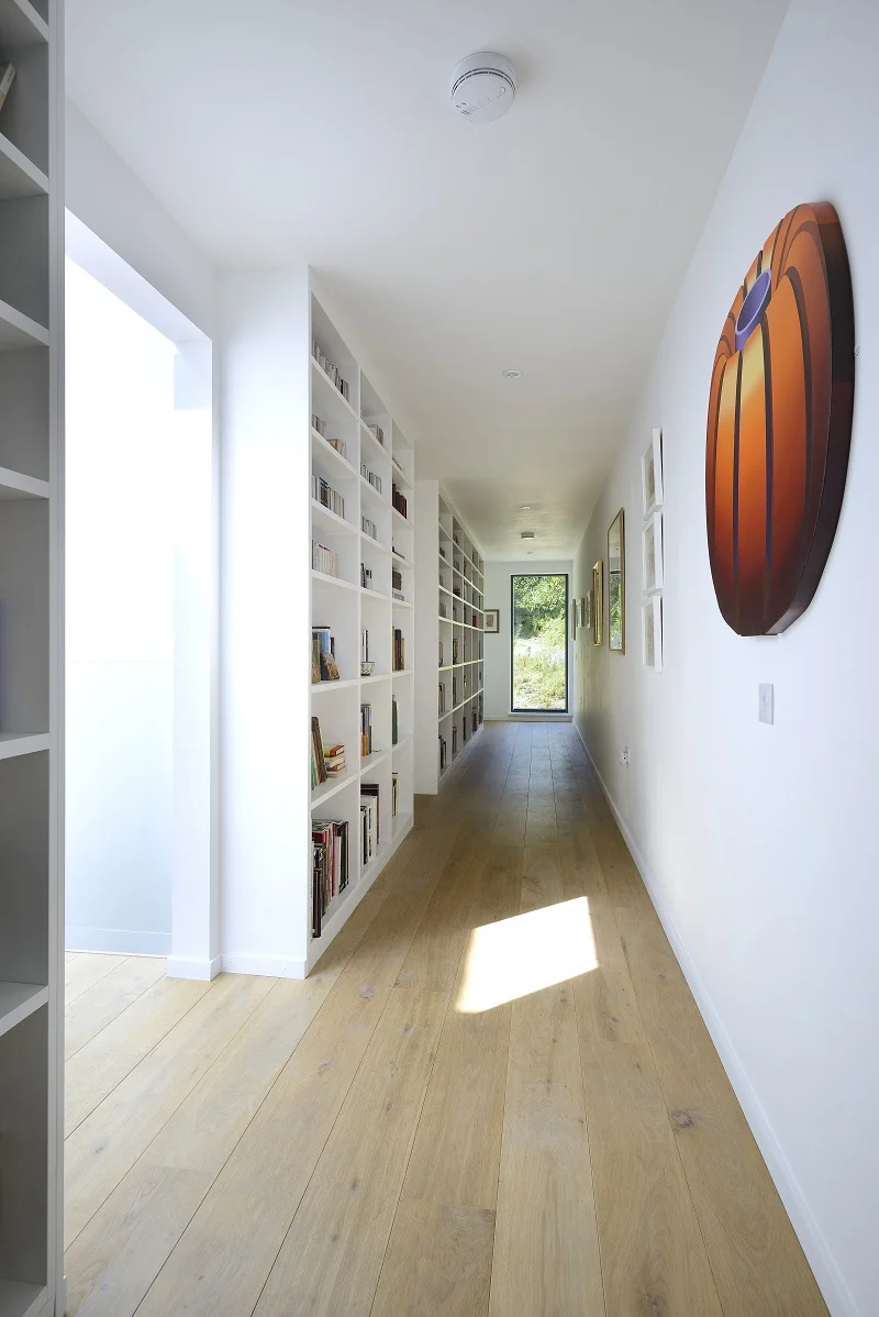Russwood Unfinished Oak Flooring hand oiled Raw Osmo in a long hallway with a large orange decorations on the wall and inbuilt shelving with a window at the end of the corridor.