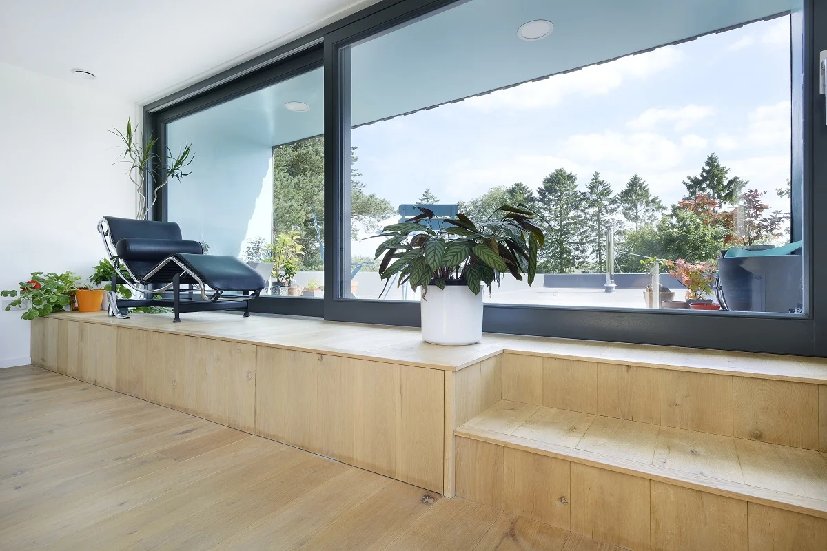 Russwood Unfinished European Oak Flooring hand oiled Raw Osmo, in a room with a large window and a plant looking out onto a patio with trees in the background.