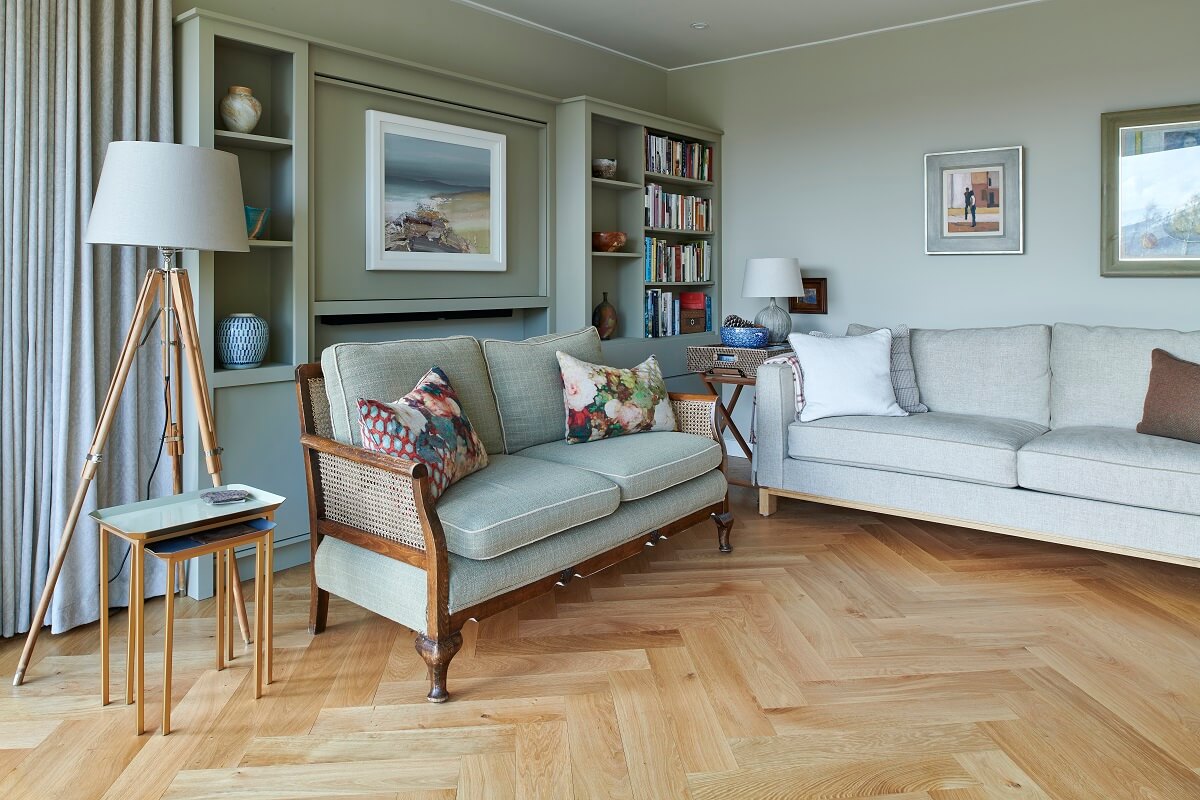 Russwood European Oak Flooring in Natural, laid in a herringbone arrangement in a modern living area with two couches and a lamp and a bookshelf.