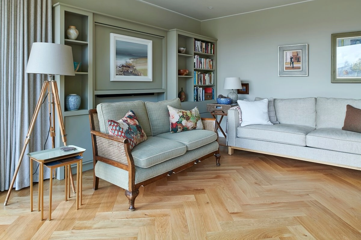 Russwood European Oak Flooring in Natural, laid in a herringbone arrangement in a modern living area with two couches and a lamp and a bookshelf.