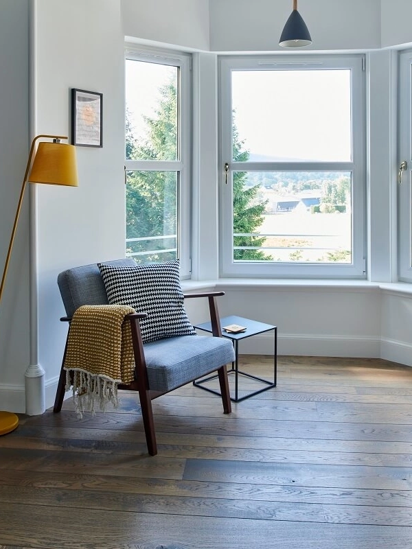 Russwood European Oak Flooring in Dusk in an apartment with a bay window and a chair with a yellow lamp.