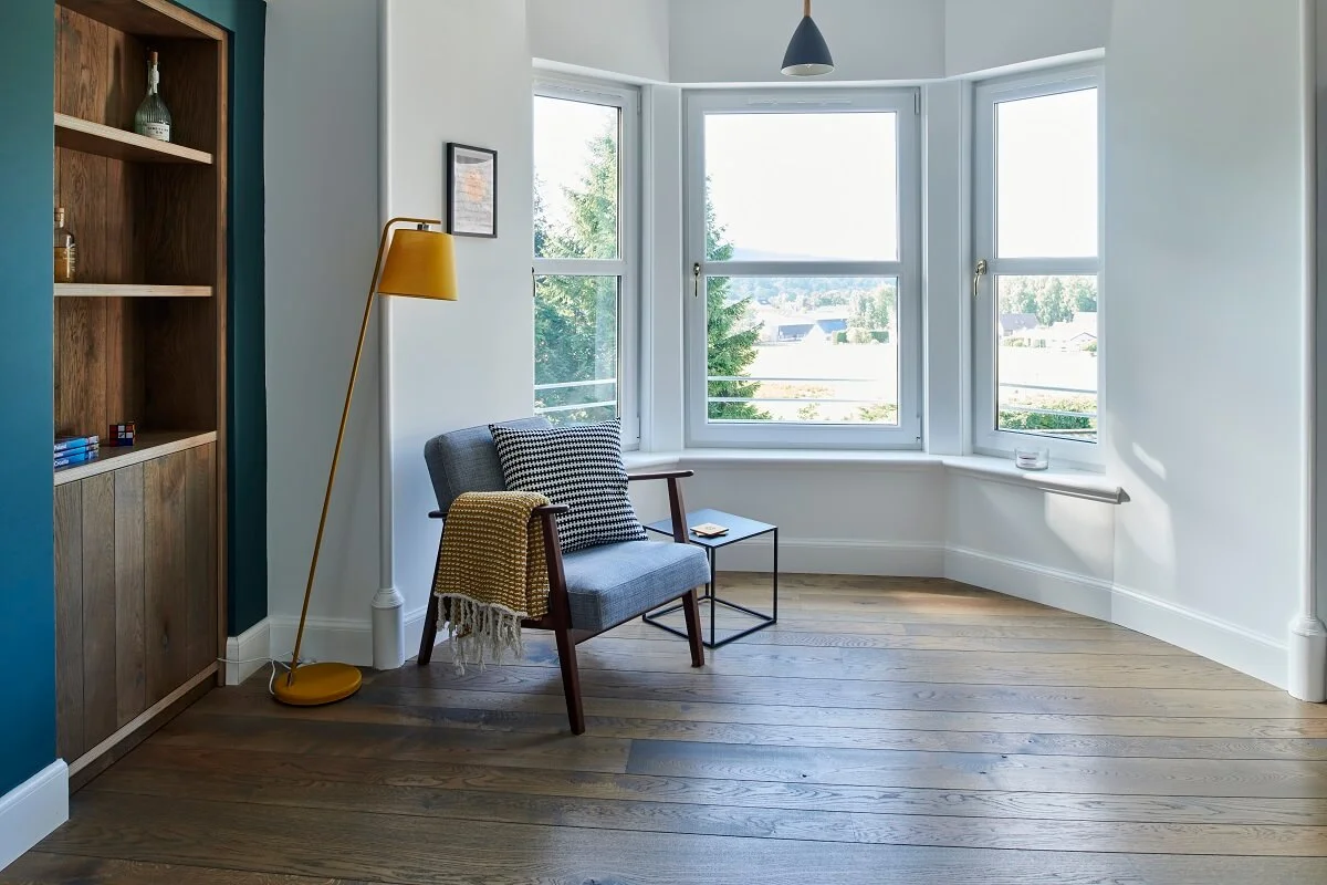 Russwood European Oak Flooring in Dusk in an apartment with a bay window and a chair with a yellow lamp.