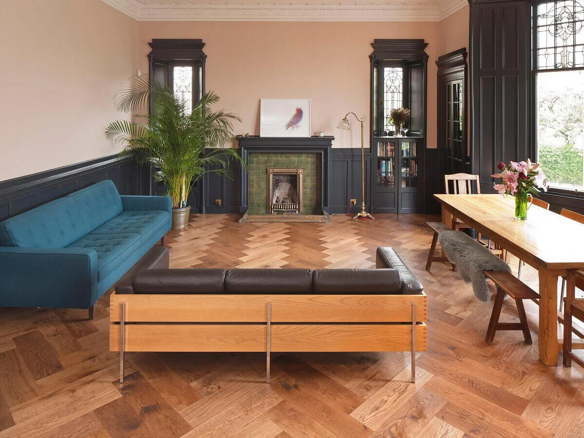 Russwood Authentic Antique Oak Flooring laid in a herringbone arrangement in a living room with couches and a large seating area, alongside plants and a fireplace.