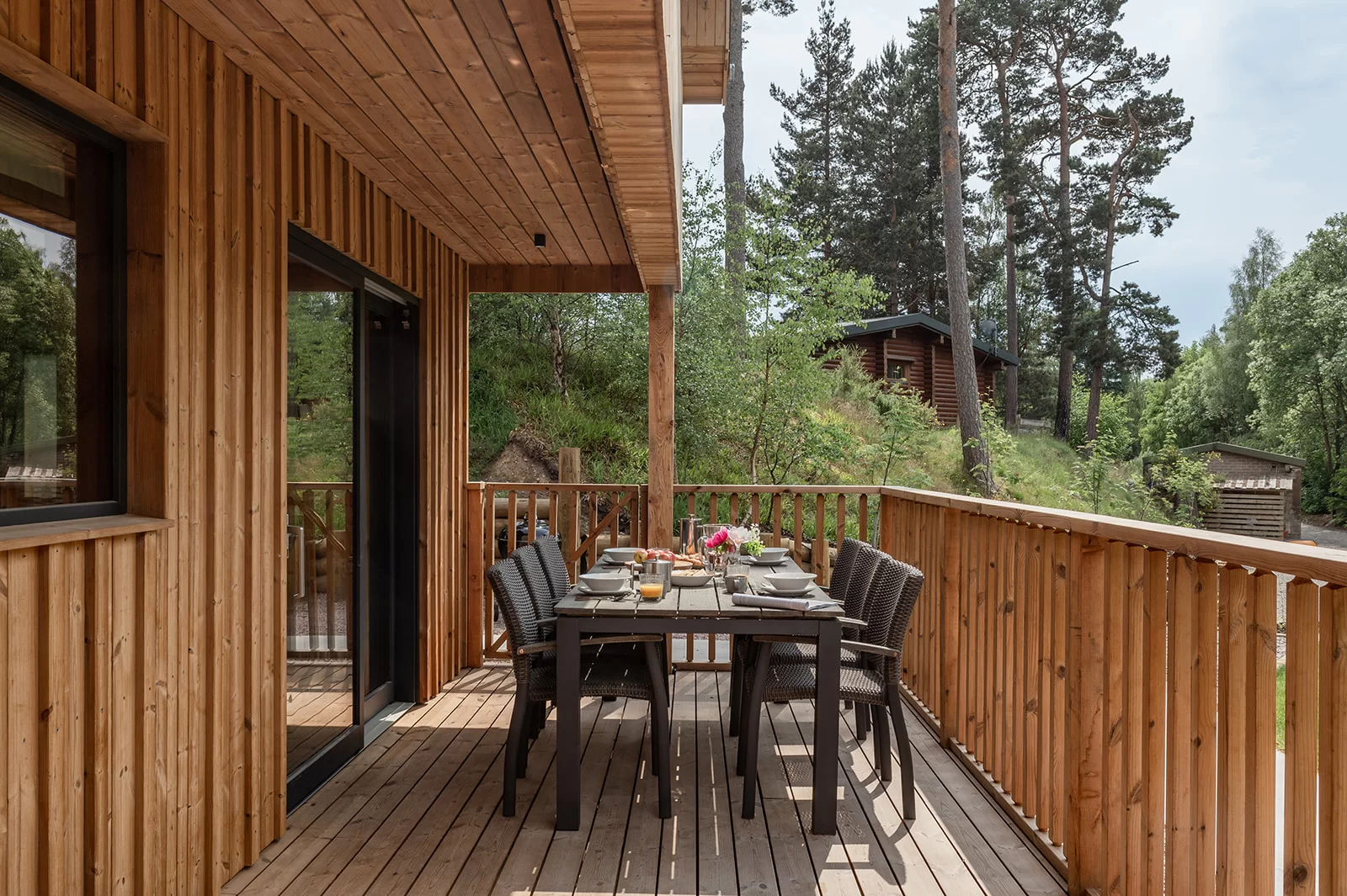 A landscape image of the pine bank chalets showing a wooden table and deck chairs sat on a Thermopine decking on a sunny day