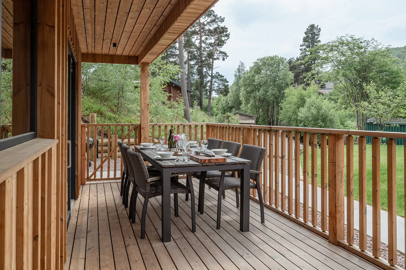 A landscape image of the pine bank chalets showing a wooden table and deck chairs sat on a Thermopine decking on a sunny day