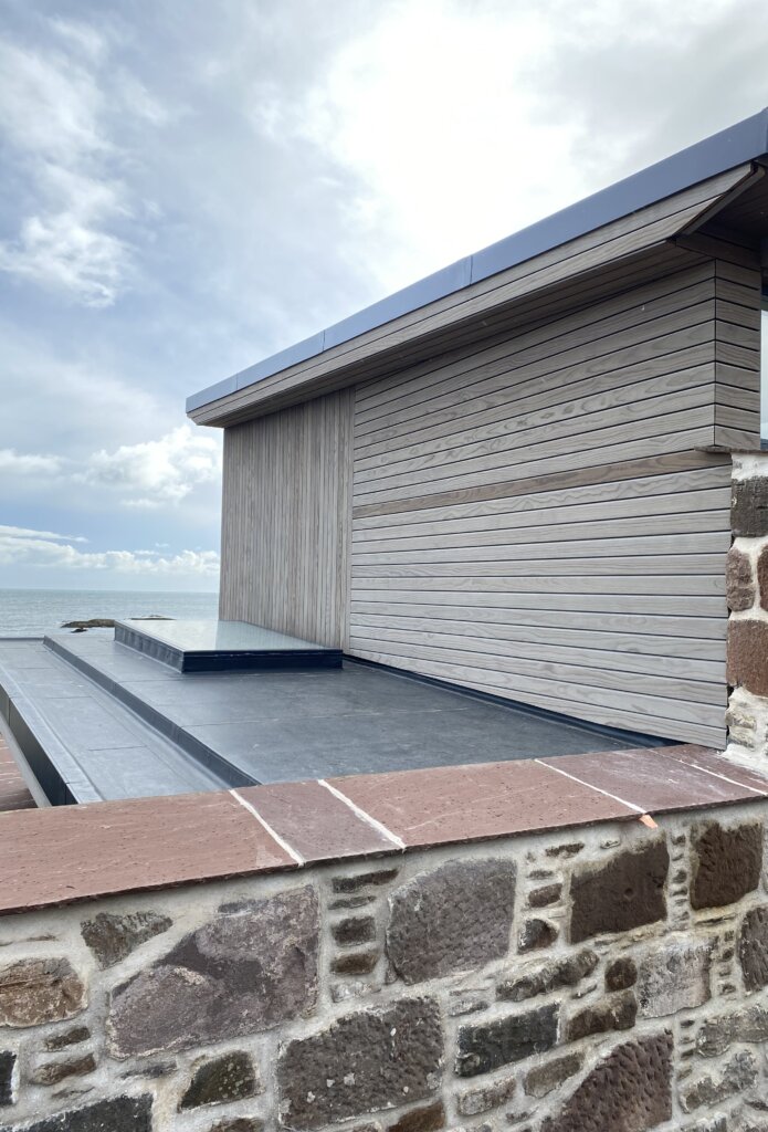 A timber clad building in front of a sea view.